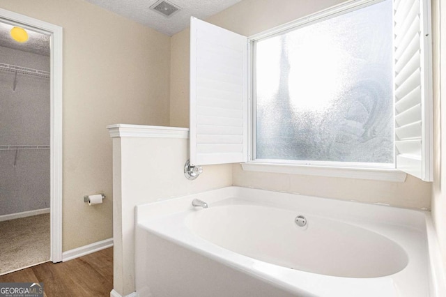 bathroom featuring visible vents, a walk in closet, wood finished floors, a bath, and a textured ceiling