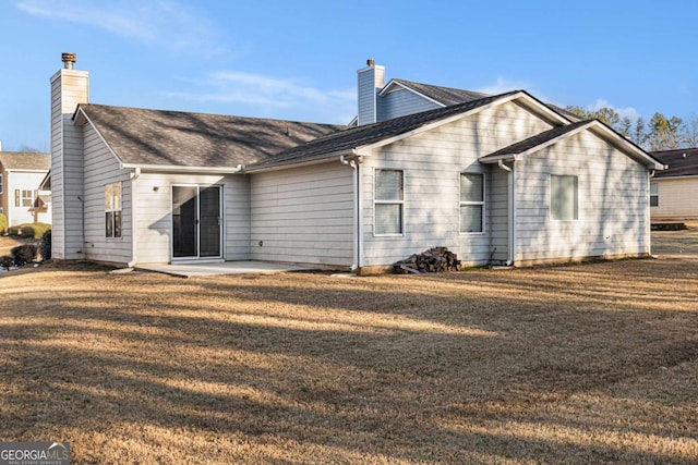 rear view of property featuring a shingled roof, a patio, a yard, and a chimney