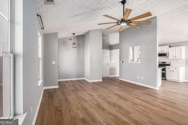 unfurnished living room featuring visible vents, baseboards, light wood-type flooring, a textured ceiling, and a ceiling fan