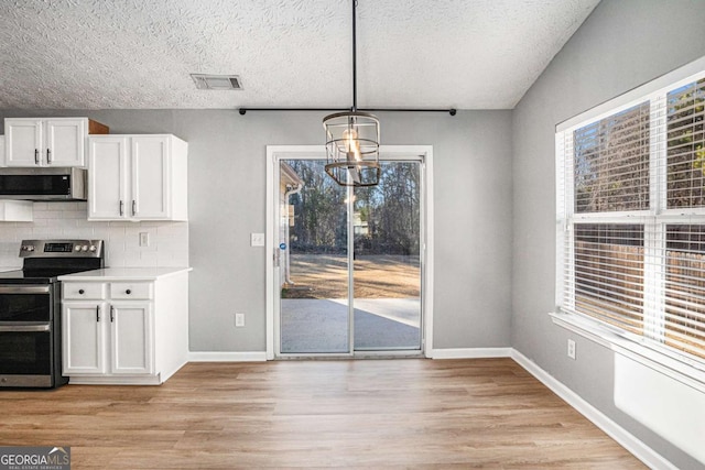 unfurnished dining area with visible vents, baseboards, a chandelier, light wood-type flooring, and a textured ceiling