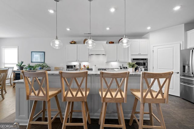 kitchen with premium range hood, an island with sink, decorative backsplash, appliances with stainless steel finishes, and white cabinetry