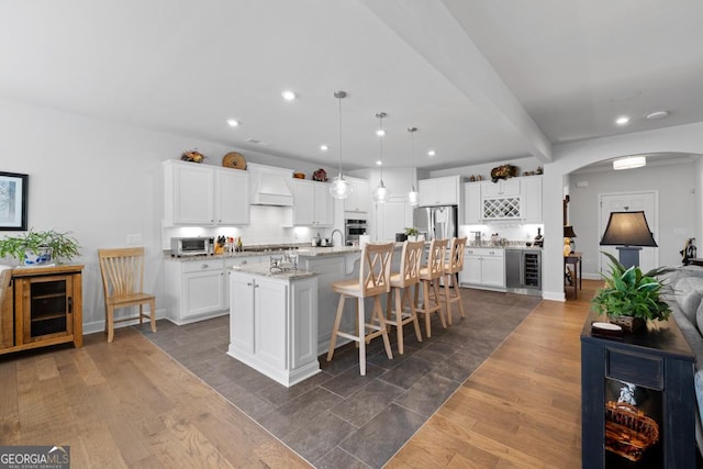 kitchen featuring beverage cooler, a kitchen bar, dark wood-style floors, arched walkways, and stainless steel appliances