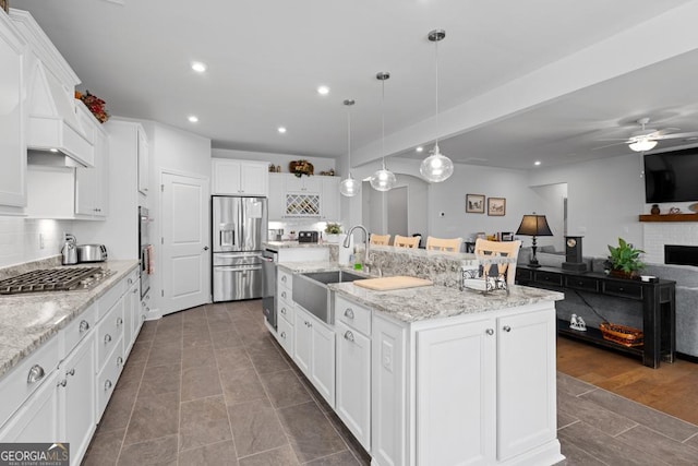 kitchen with a center island with sink, a sink, backsplash, white cabinetry, and appliances with stainless steel finishes