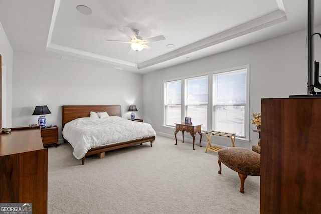 bedroom with a raised ceiling, a ceiling fan, baseboards, and light carpet