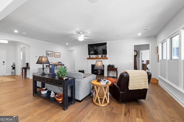 living room with arched walkways, recessed lighting, a brick fireplace, and wood finished floors