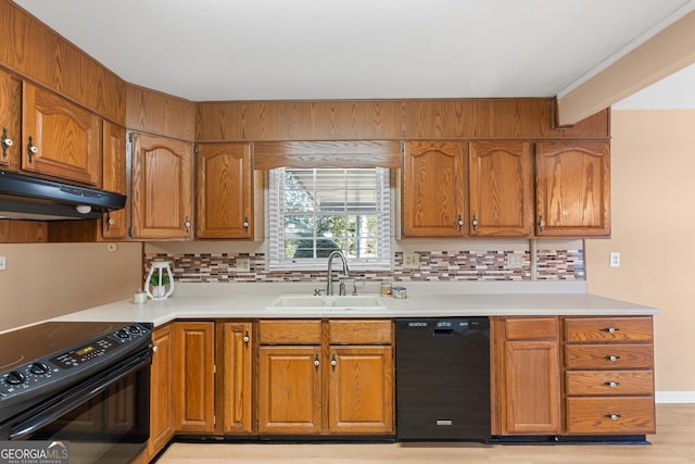 kitchen with tasteful backsplash, light countertops, a sink, under cabinet range hood, and black appliances