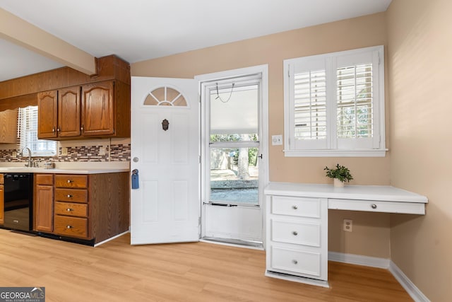 kitchen featuring light wood finished floors, brown cabinetry, dishwasher, built in study area, and light countertops