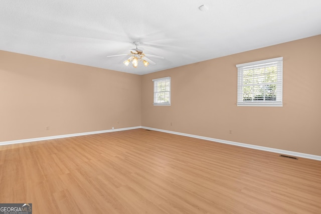 empty room featuring light wood-style flooring, visible vents, baseboards, and a ceiling fan