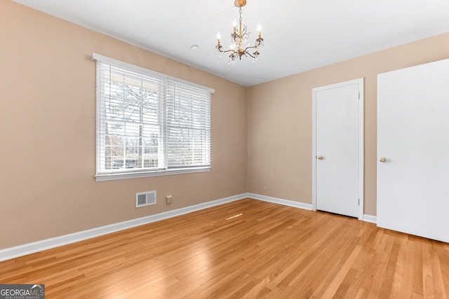 spare room featuring baseboards, visible vents, light wood finished floors, and an inviting chandelier