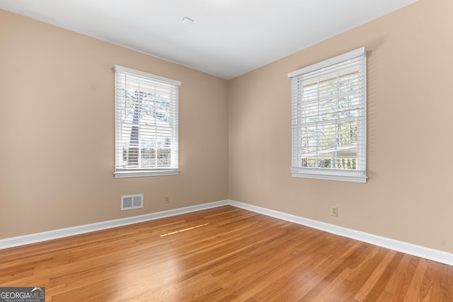 empty room featuring light wood-style floors, visible vents, and baseboards