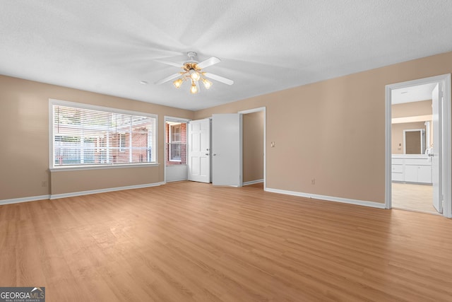 unfurnished bedroom featuring baseboards, connected bathroom, light wood-style flooring, ceiling fan, and a textured ceiling