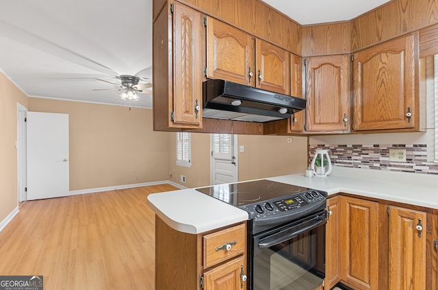 kitchen with under cabinet range hood, backsplash, brown cabinets, and black electric range oven