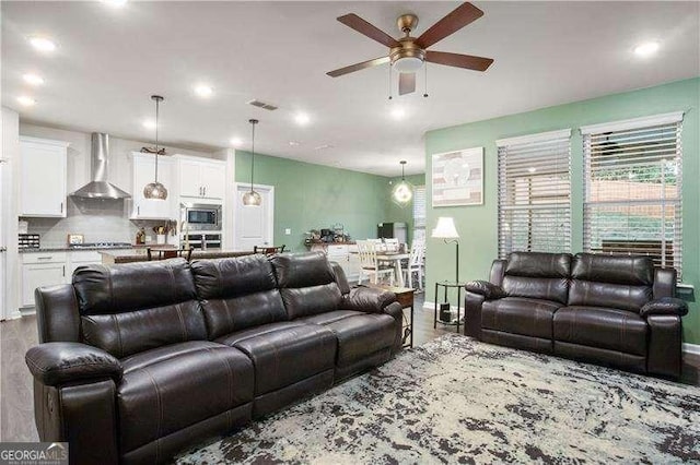 living area featuring baseboards, wood finished floors, visible vents, and a ceiling fan