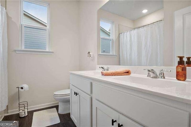 full bath featuring double vanity, a sink, toilet, and baseboards