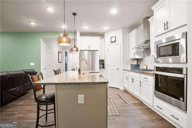 kitchen with a breakfast bar area, white cabinetry, appliances with stainless steel finishes, wall chimney range hood, and dark wood finished floors