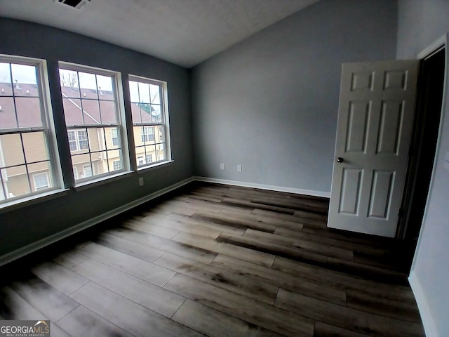 spare room featuring dark wood-style floors, lofted ceiling, and baseboards