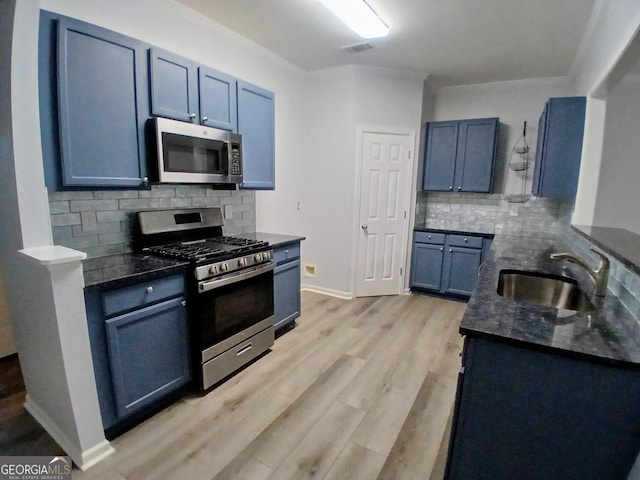 kitchen with tasteful backsplash, appliances with stainless steel finishes, dark stone countertops, light wood-type flooring, and a sink