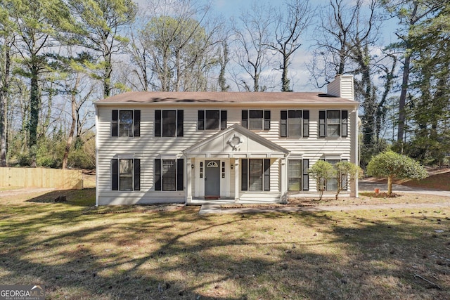 colonial-style house featuring a chimney, fence, and a front yard