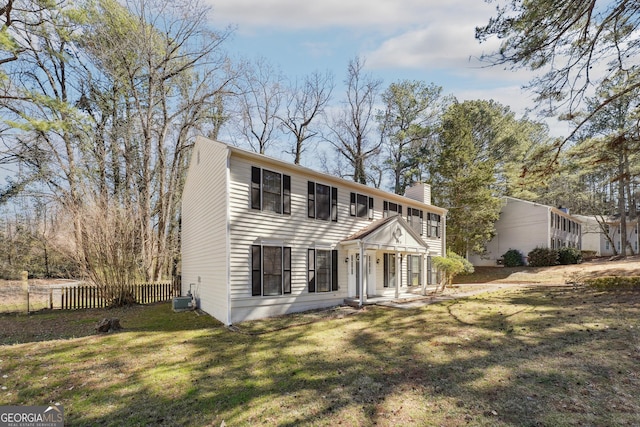 colonial house with a front yard, fence, a chimney, and central AC unit