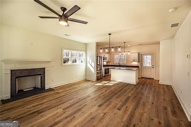 unfurnished living room featuring a wealth of natural light, dark wood-type flooring, a fireplace with flush hearth, and visible vents