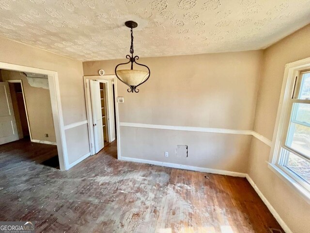 unfurnished dining area featuring plenty of natural light, a textured ceiling, baseboards, and wood finished floors