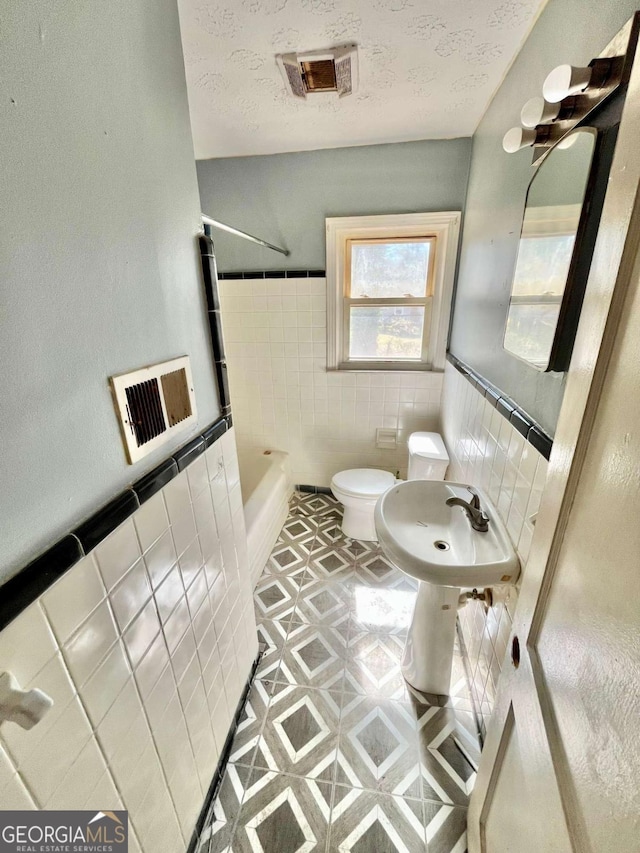 full bath with toilet, a textured ceiling, visible vents, and tile walls