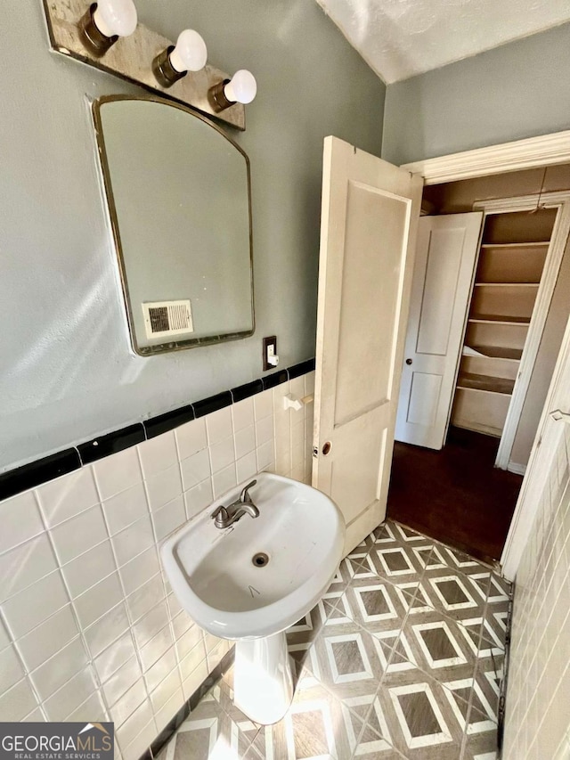 bathroom featuring visible vents, a wainscoted wall, a sink, and tile walls