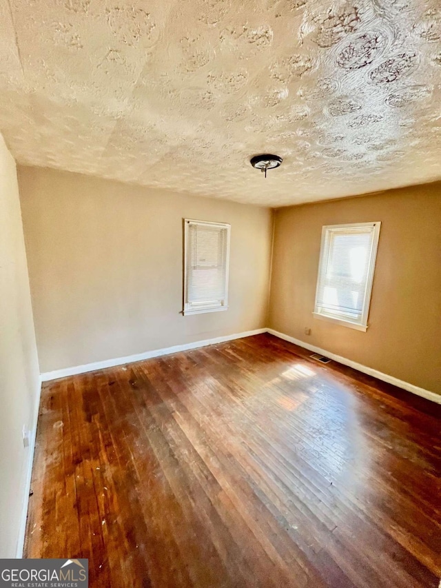 unfurnished room with wood-type flooring, visible vents, baseboards, and a textured ceiling