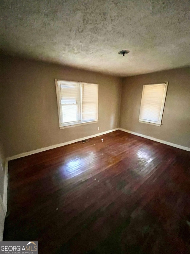 spare room with a textured ceiling, baseboards, and wood finished floors