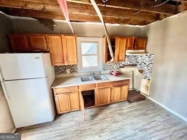 kitchen with light countertops, backsplash, freestanding refrigerator, a sink, and light wood-type flooring