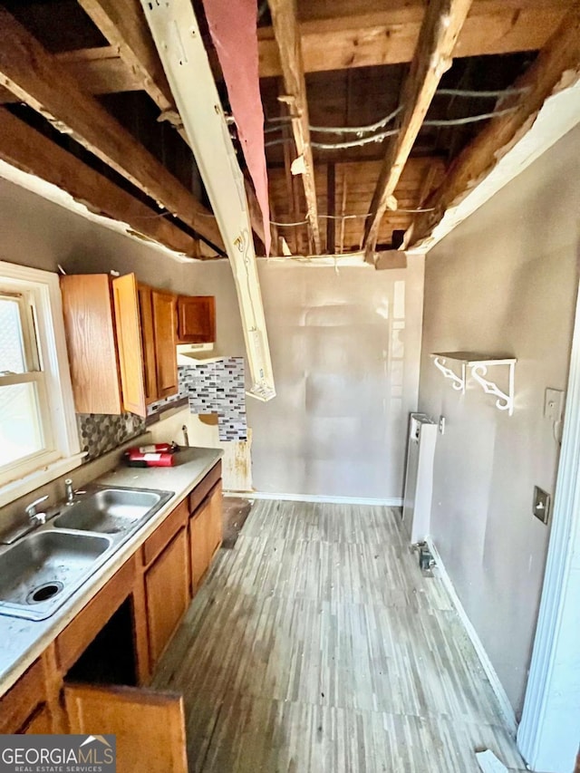 kitchen featuring brown cabinetry, radiator heating unit, wood finished floors, a sink, and backsplash