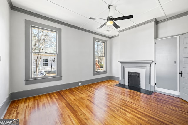 unfurnished living room featuring hardwood / wood-style floors, baseboards, a fireplace with raised hearth, and crown molding