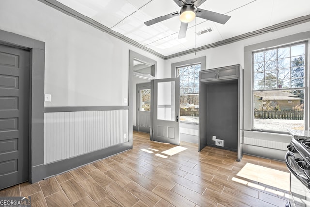 interior space featuring wood finish floors, a ceiling fan, visible vents, wainscoting, and crown molding