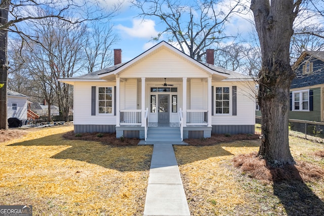 bungalow-style home with a chimney, a porch, a front lawn, and a shingled roof