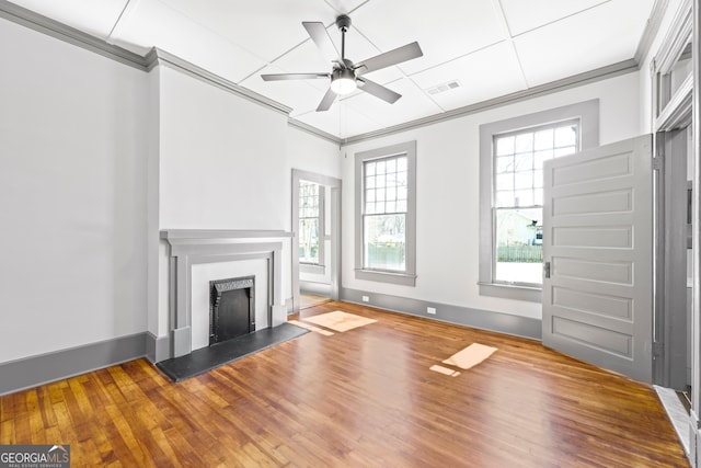 unfurnished living room with a fireplace with raised hearth, wood finished floors, a wealth of natural light, and crown molding