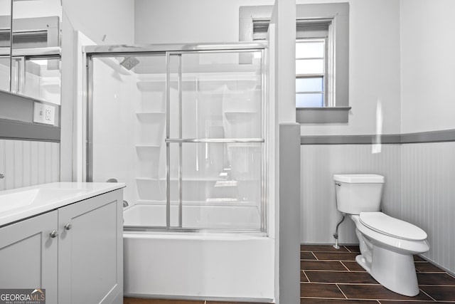 full bathroom featuring enclosed tub / shower combo, toilet, wood finish floors, vanity, and wainscoting