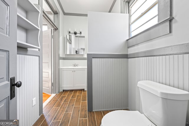 bathroom with toilet, vanity, ornamental molding, wainscoting, and wood tiled floor