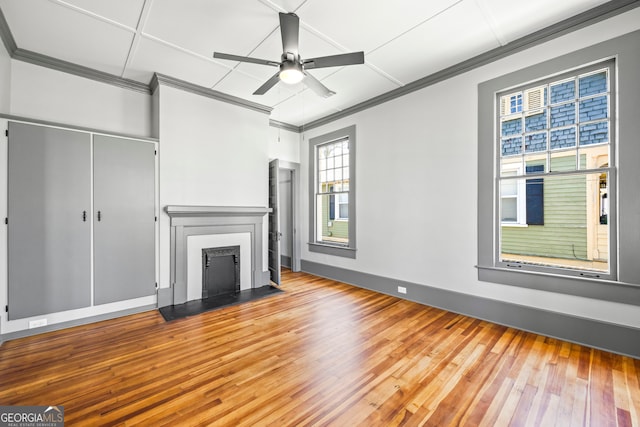 unfurnished living room featuring baseboards, a fireplace with flush hearth, ceiling fan, hardwood / wood-style floors, and crown molding