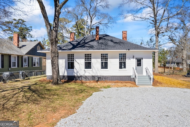 back of house featuring gravel driveway, a chimney, fence, and a yard
