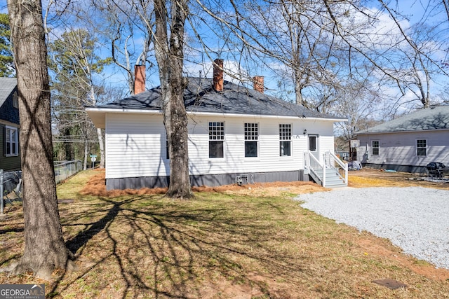 rear view of property featuring a chimney, a lawn, gravel driveway, and fence