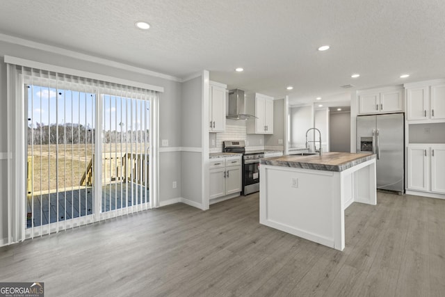 kitchen with appliances with stainless steel finishes, light wood-style floors, white cabinetry, a sink, and wall chimney range hood