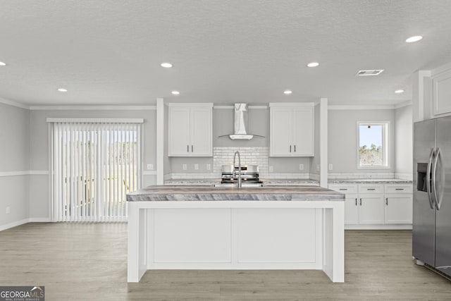 kitchen with tasteful backsplash, stainless steel fridge, light wood-style flooring, light countertops, and wall chimney range hood