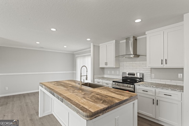 kitchen with a kitchen island with sink, a sink, white cabinets, wall chimney range hood, and stainless steel electric stove