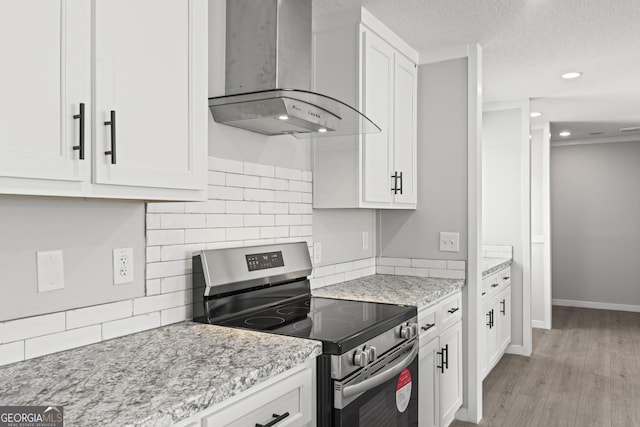 kitchen with wall chimney range hood, stainless steel electric range, and white cabinetry