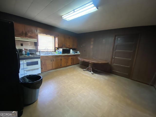 kitchen featuring brown cabinets, light floors, a sink, white range with gas stovetop, and under cabinet range hood