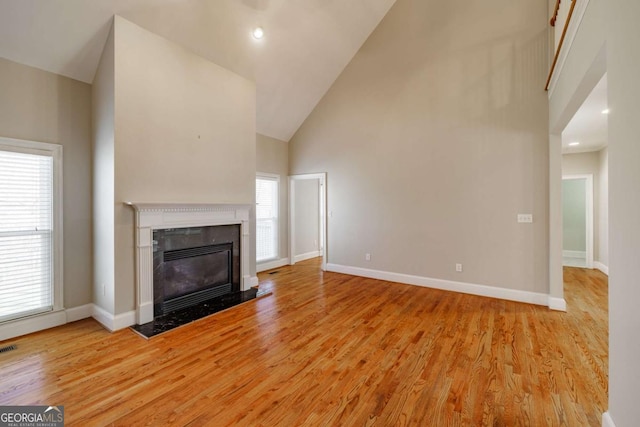 unfurnished living room with high vaulted ceiling, a high end fireplace, light wood-style flooring, and baseboards