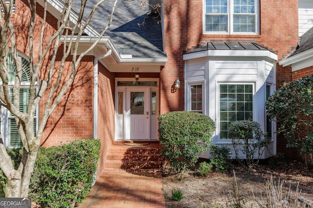 entrance to property featuring a shingled roof and brick siding