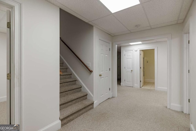 interior space featuring baseboards, a drop ceiling, stairs, and light colored carpet