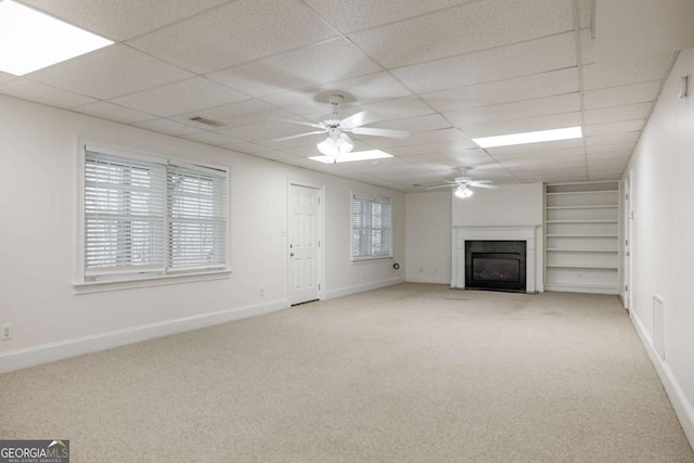 unfurnished living room featuring baseboards, a fireplace with flush hearth, a ceiling fan, and light colored carpet