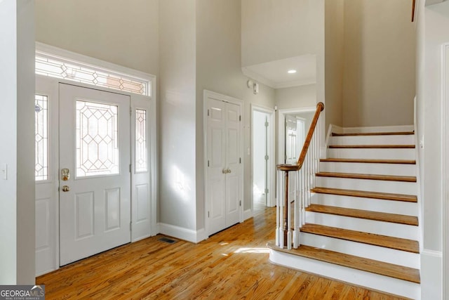 entrance foyer with visible vents, stairway, a towering ceiling, light wood-type flooring, and baseboards